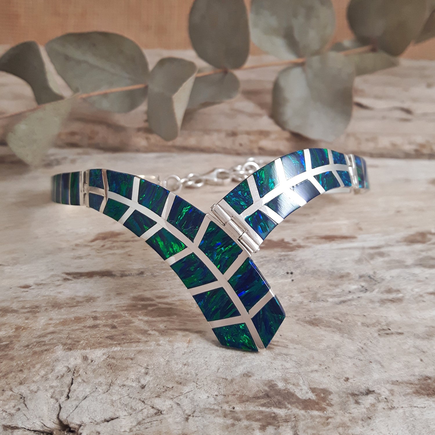 Cultured emerald opal and sterling silver geometric bracelet on a wooden surface with eucalyptus leaves in the background