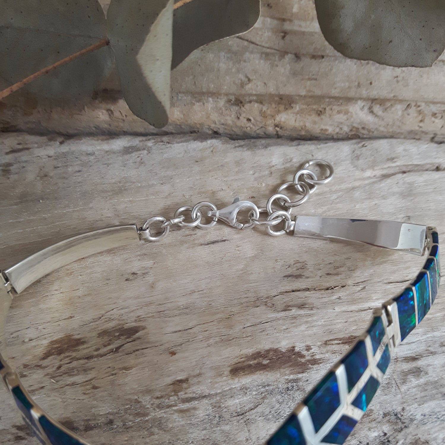 Sterling silver bracelet with a emerald cultured opal band on a wooden surface