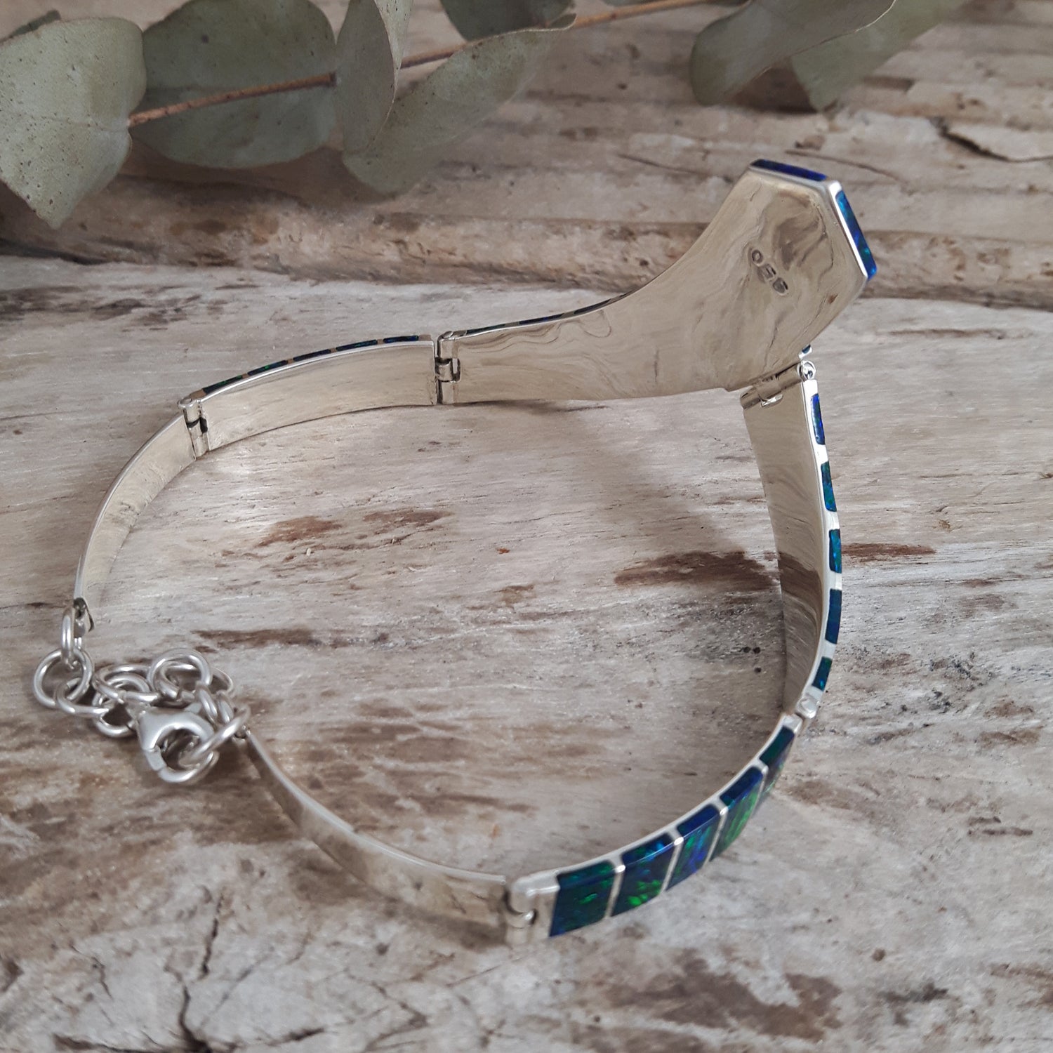 Sterling silver bracelet with emerald cultured opal inlay on a wooden surface