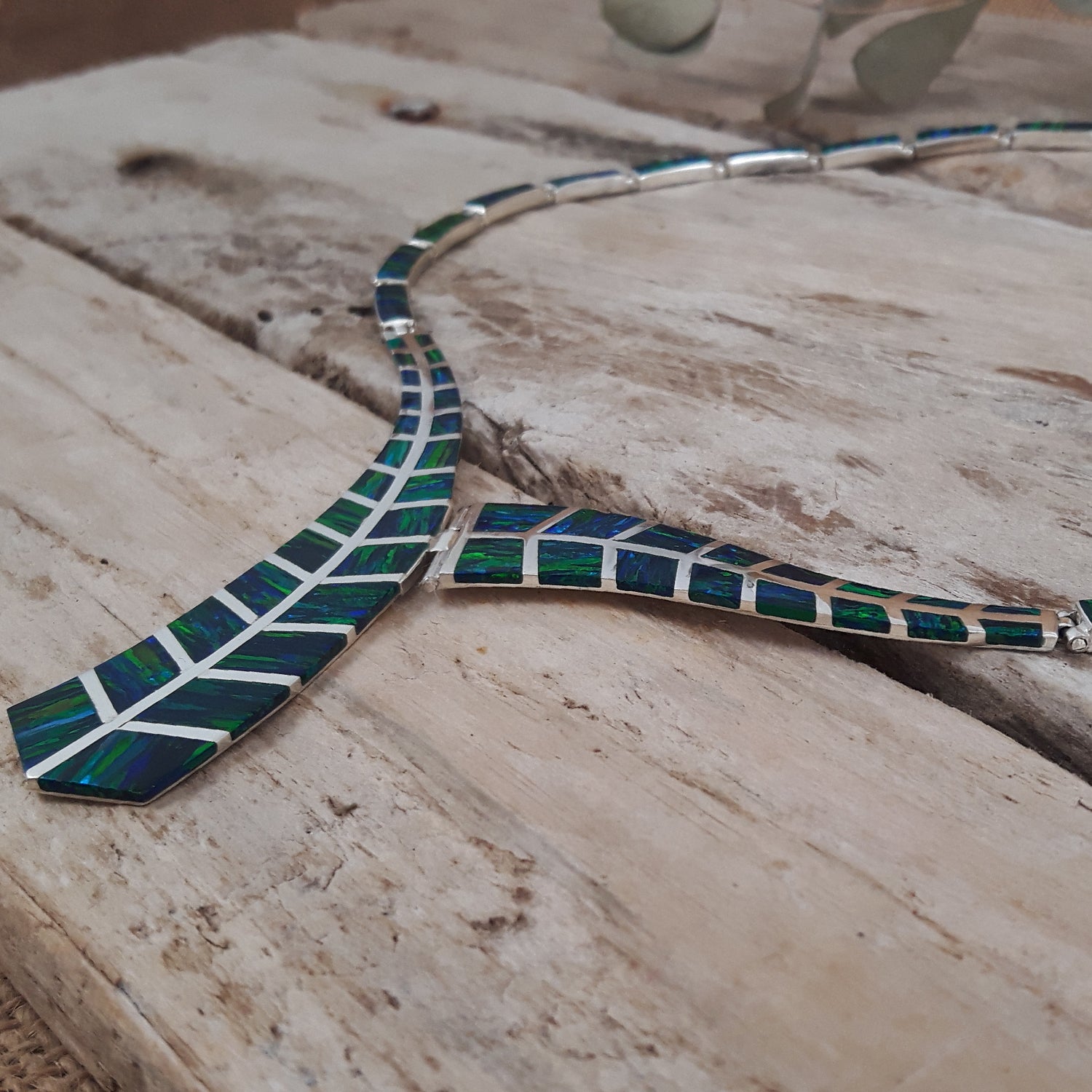 Sterling silver necklace with emerald cultured opal detail on a wooden surface