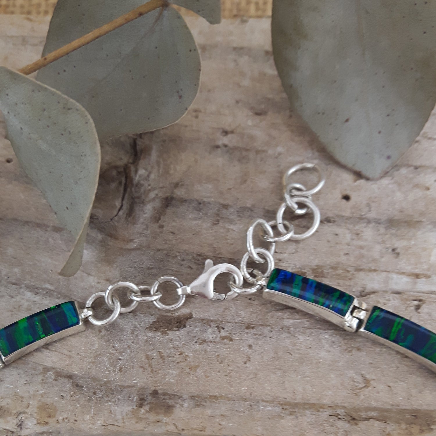 Sterling silver necklace with emerald cultured opal inlay on a wooden surface with leaves in the background