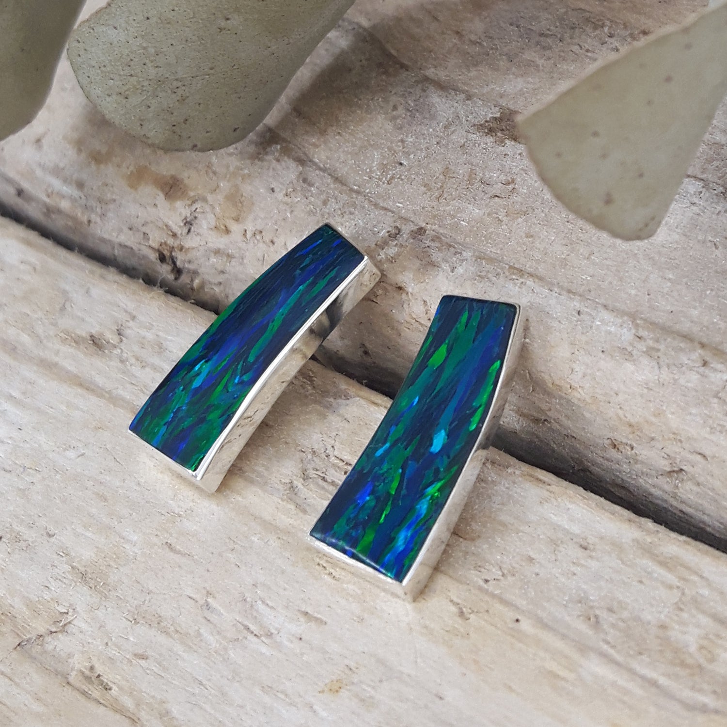 Rio cultured opal emerald stud earrings on a wooden surface
