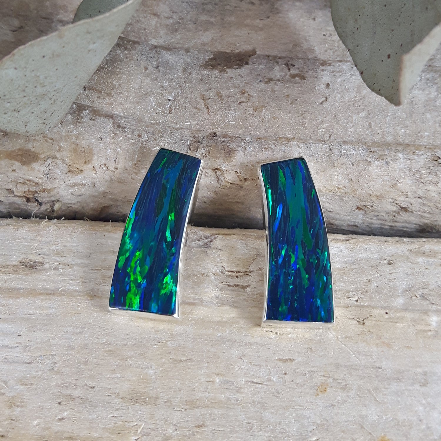 Pair of Flinder Rio cultured opal stud earrings in emerald with colourful design on a wooden surface