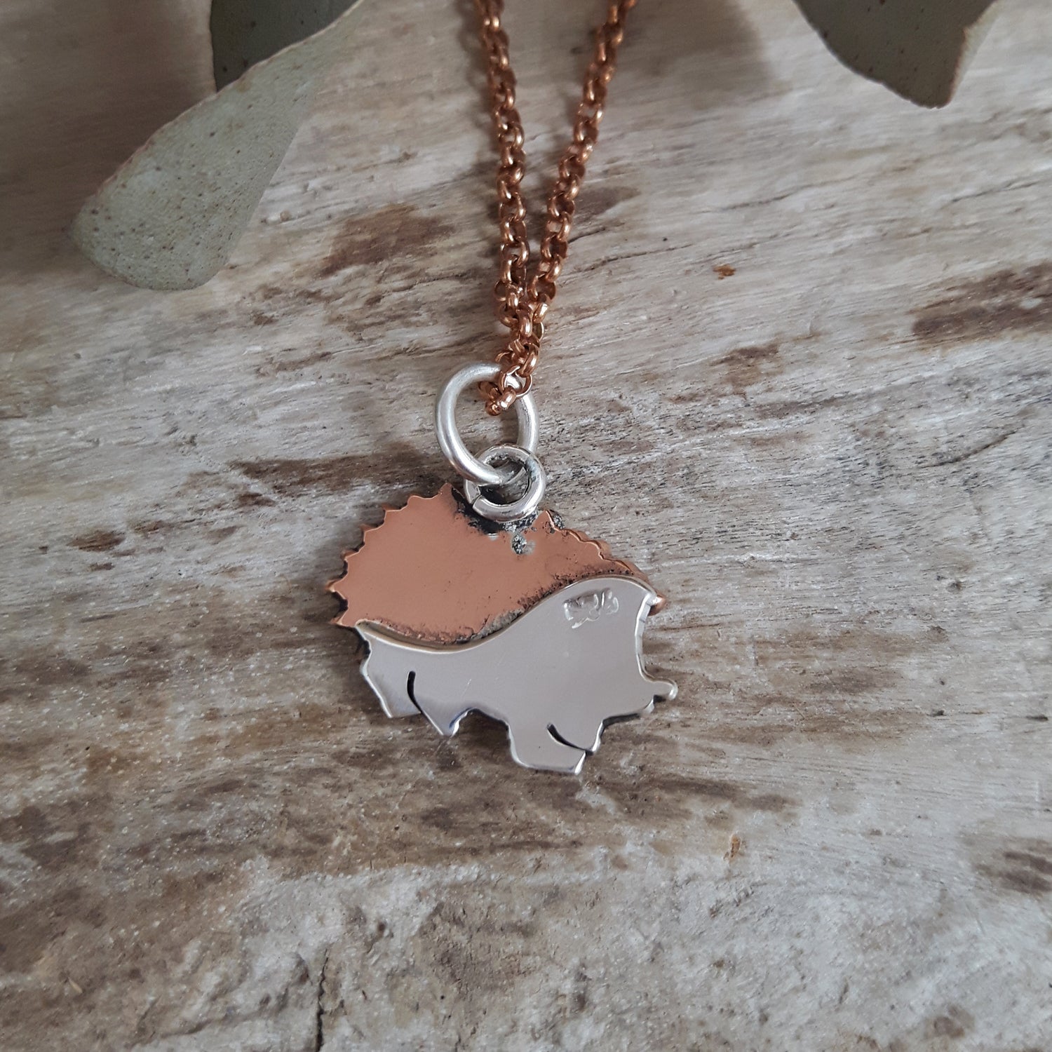 Rose gold chain with a handcrafted sterling silver and copper hedgehog pendant on a wooden surface