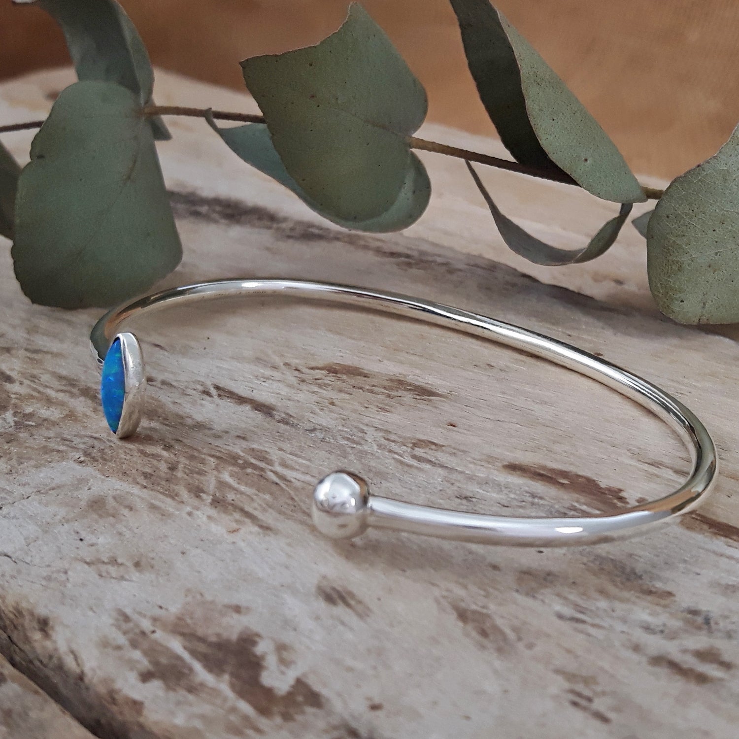 Silver cuff bracelet with a turquoise opalite stone on a wooden surface with leaves in the background