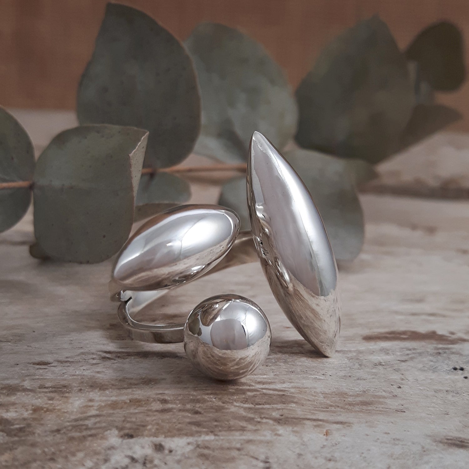 Handmade sterling silver Maya ring on a wooden surface with eucalyptus leaves in the background