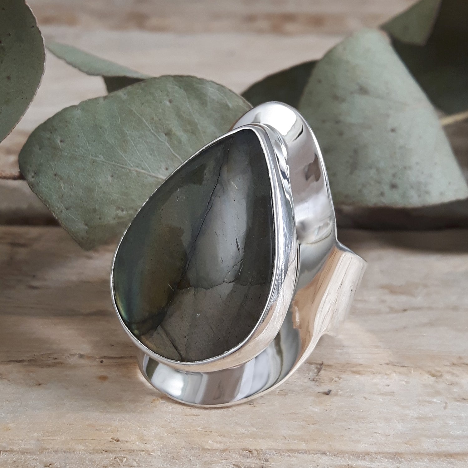 Silver ring with a labradorite stone on a wooden surface with leaves in the background