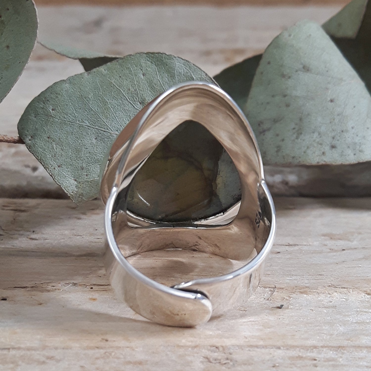 Silver ring with a textured design on a wooden surface with green leaves in the background