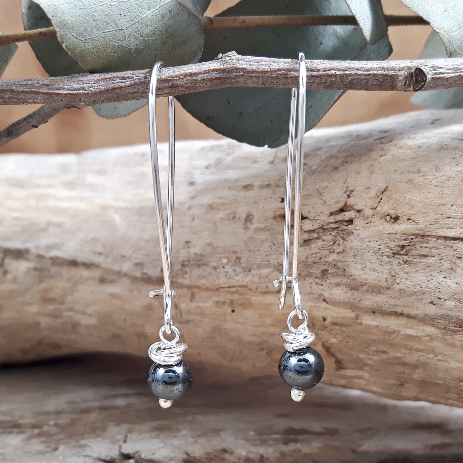 Sterling silver earrings with dark hematite beads hanging on a branch with leaves in the background