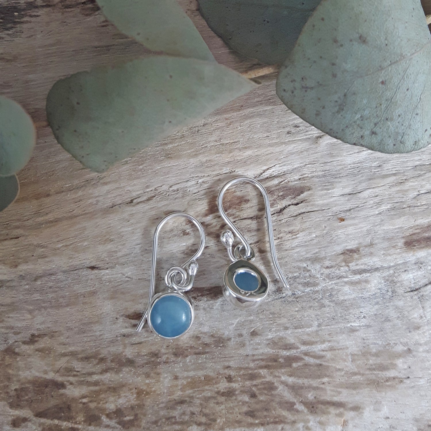 Silver earrings with aquamarine gemstones on a wooden surface with green leaves.