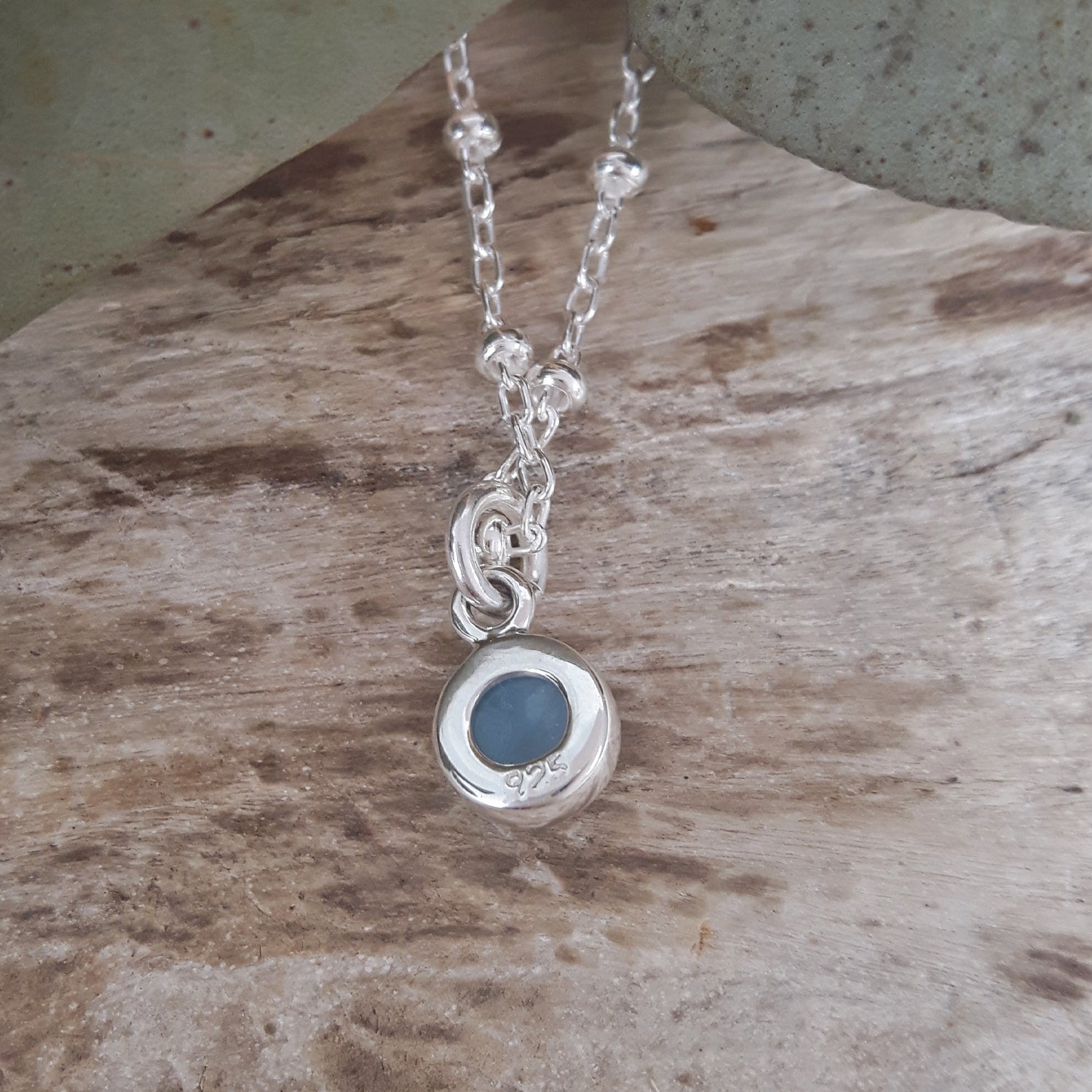 Silver necklace with a blue pendant on a wooden surface
