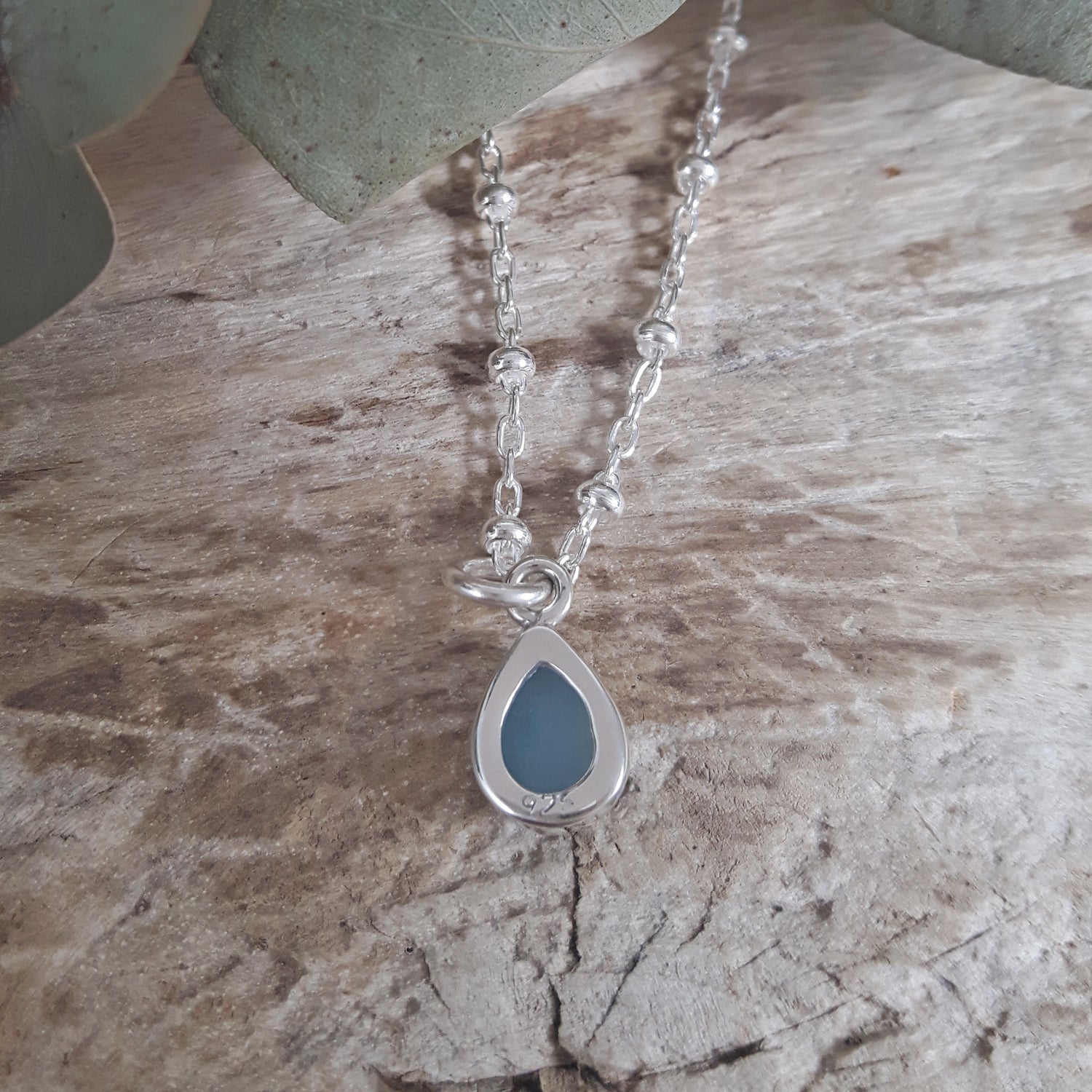 Silver chain necklace with an aquamarine teardrop pendant on a textured stone surface
