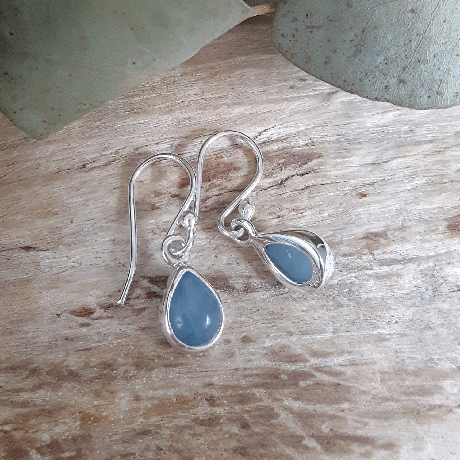 Silver earrings with aquamarine teardrop gemstones on a wooden surface