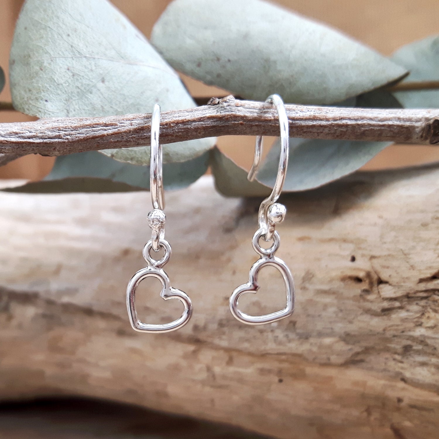 Silver open heart-shaped sterling silver earrings on a branch with a natural background