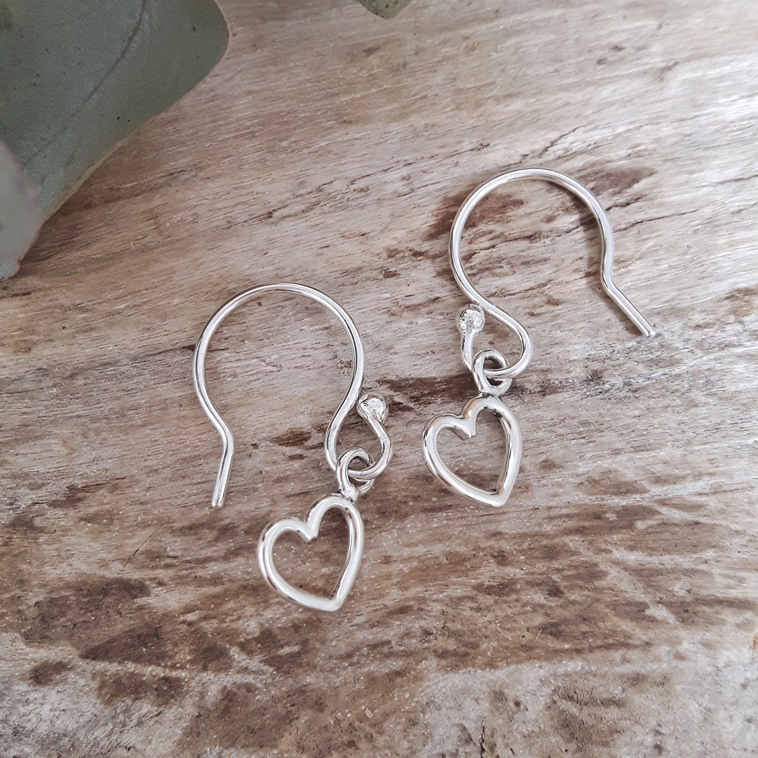 Sterling silver heart-shaped earrings on a wooden surface, artisan-made, designed in the UK. Gifts under £35