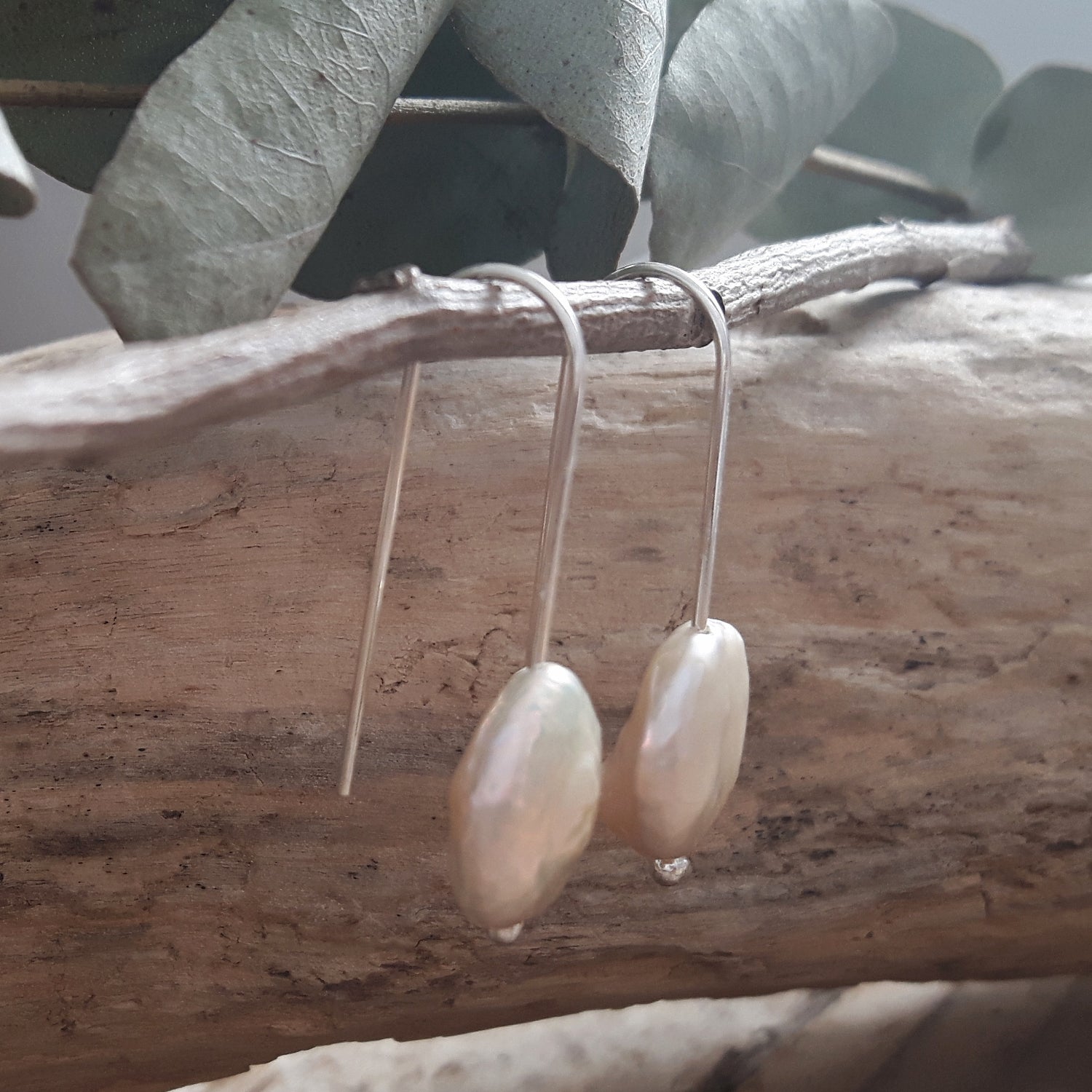 Pearl earrings hanging on a branch with leaves in the background