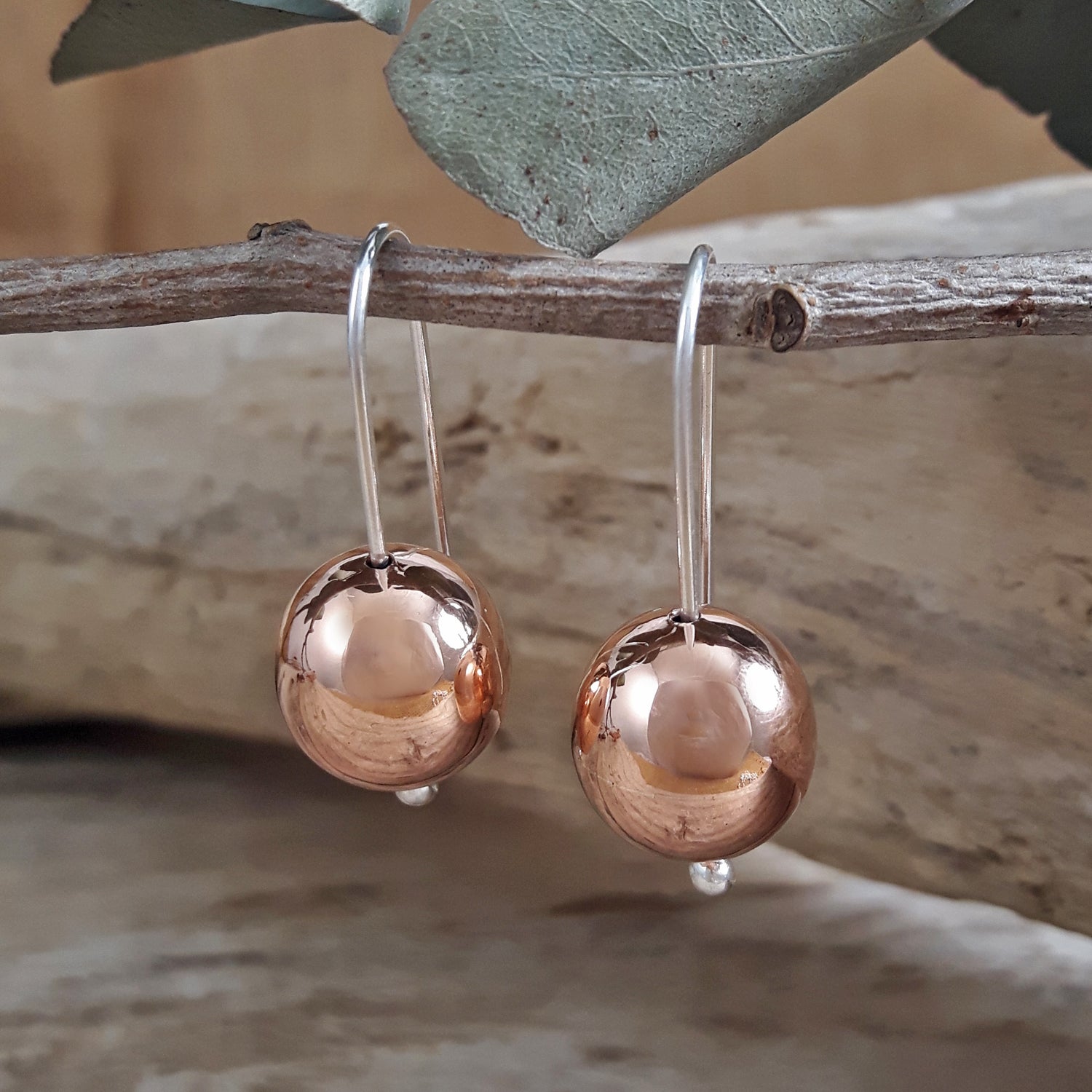 Copper ball earrings hanging from a branch with a natural background
