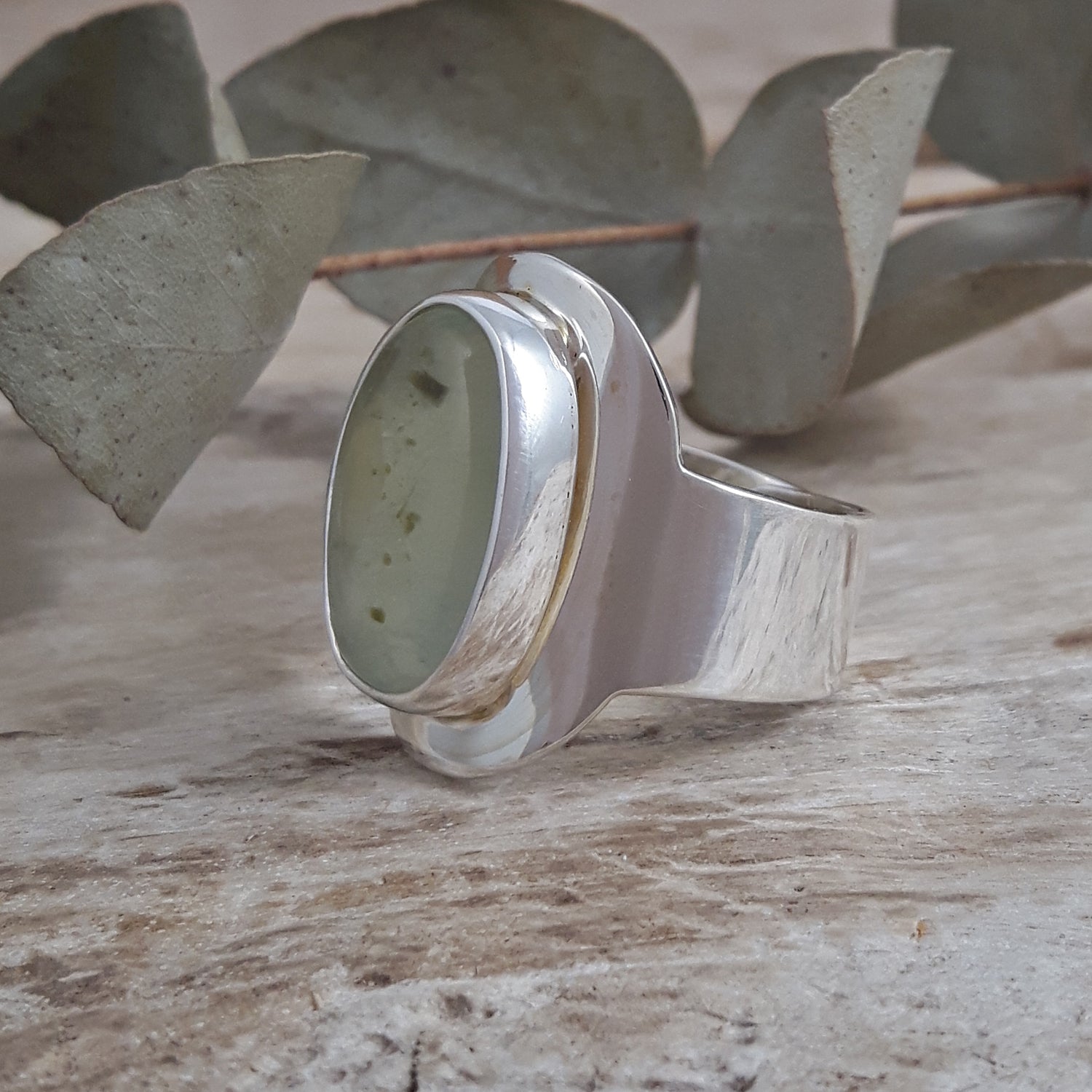 Sterling silver gemstone ring on a wooden surface with eucalyptus leaves in the background