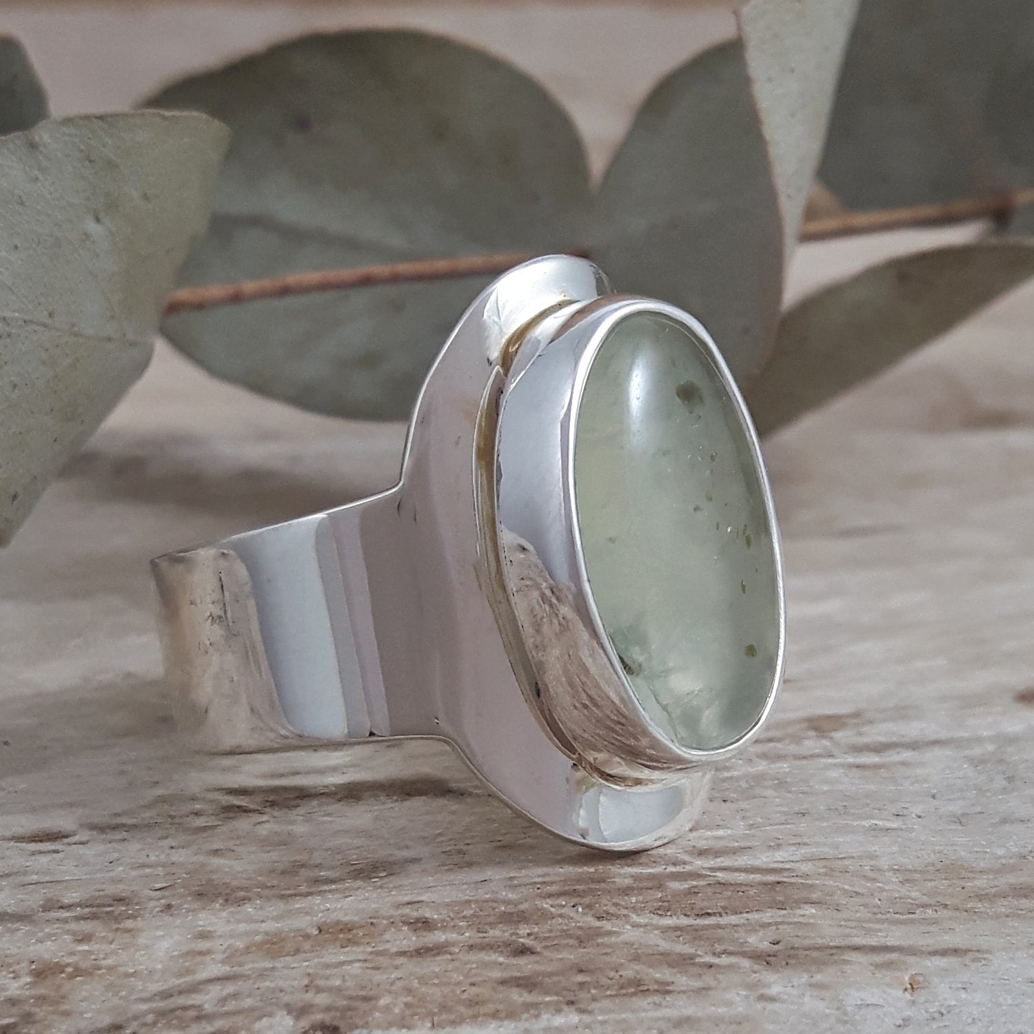 Sterling silver ring with a green prehnite gemstone on a wooden surface with leaves