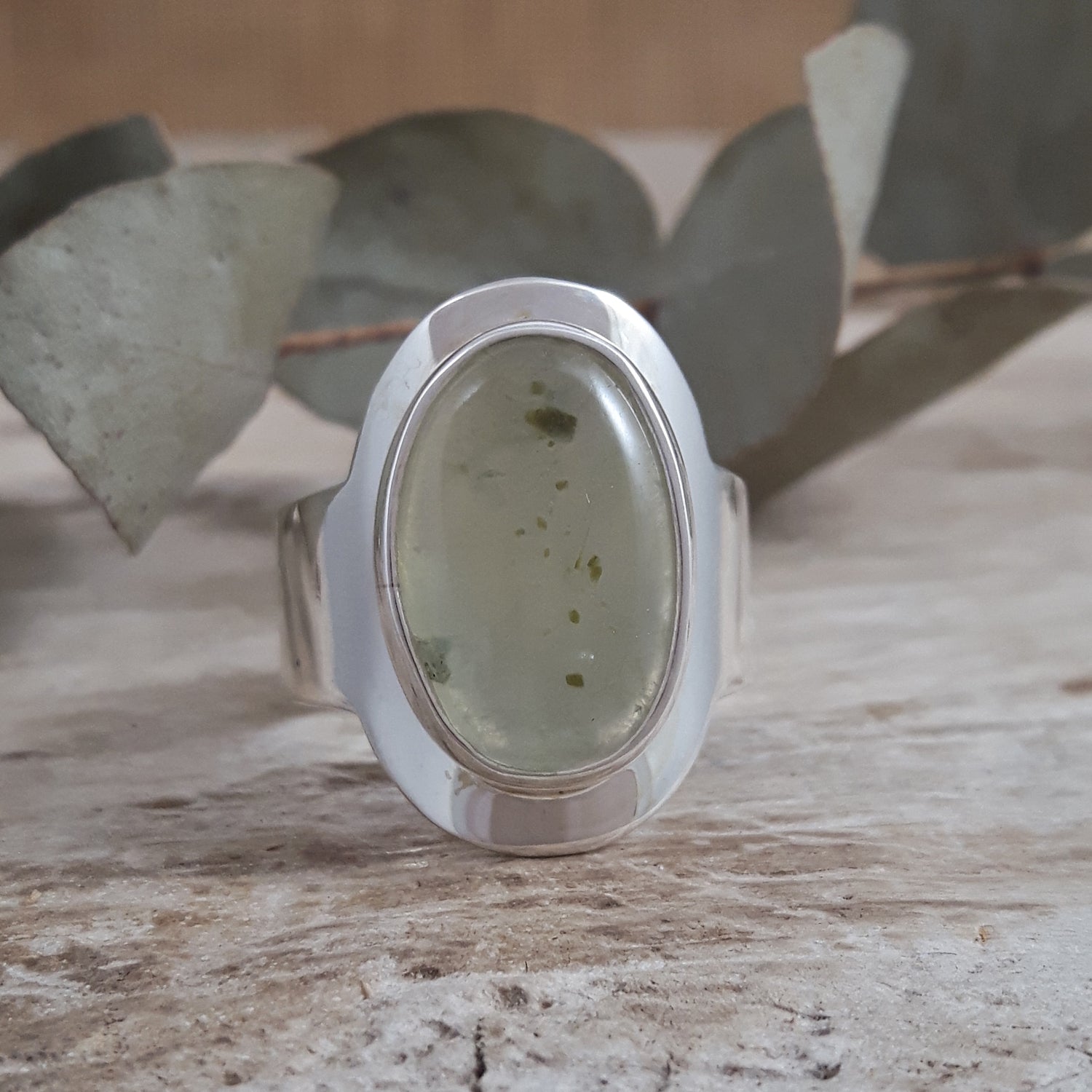 Sterling silver ring with a green prehnite stone on a wooden surface with leaves in the background
