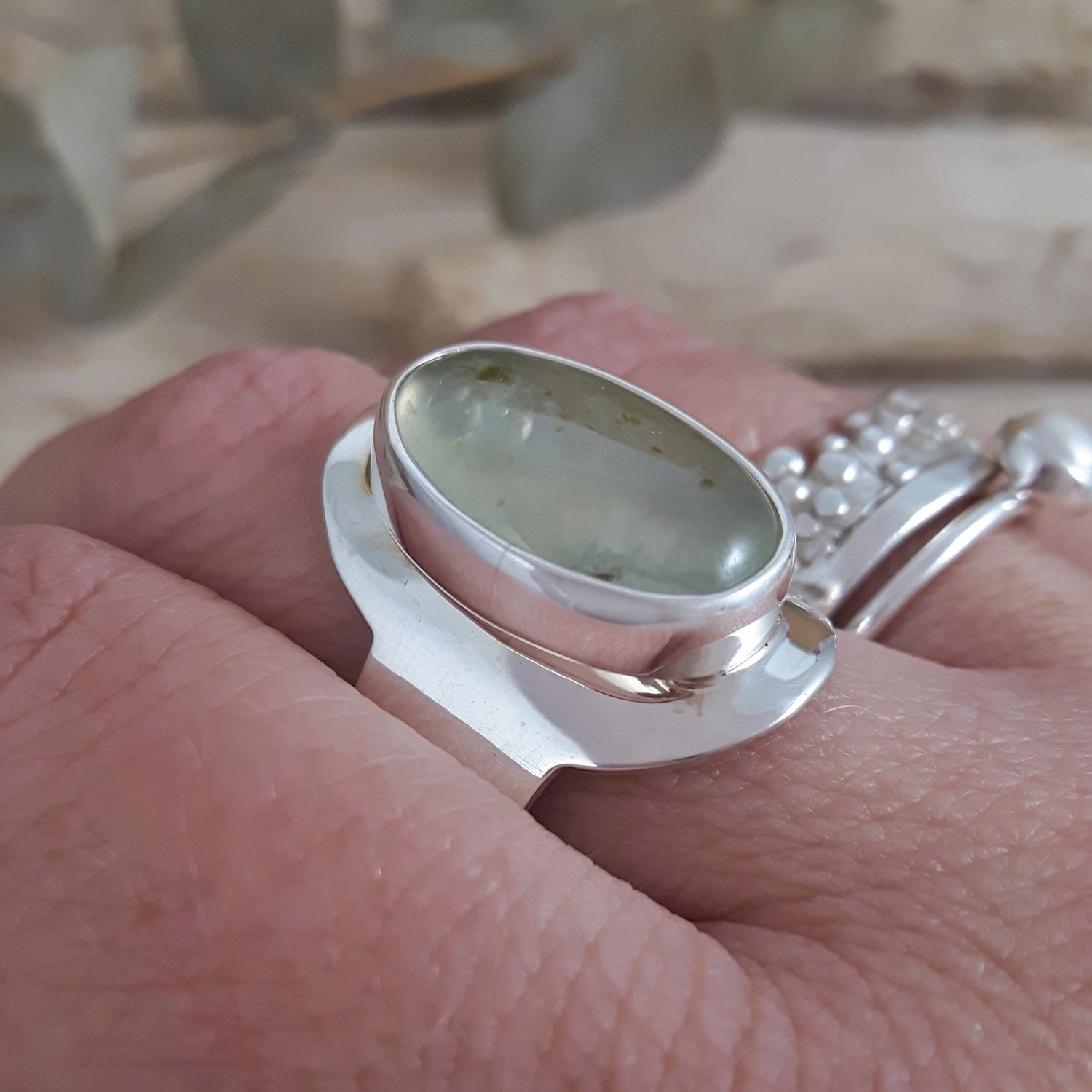 Sterling silver ring with a green prehnite stone on a person's finger