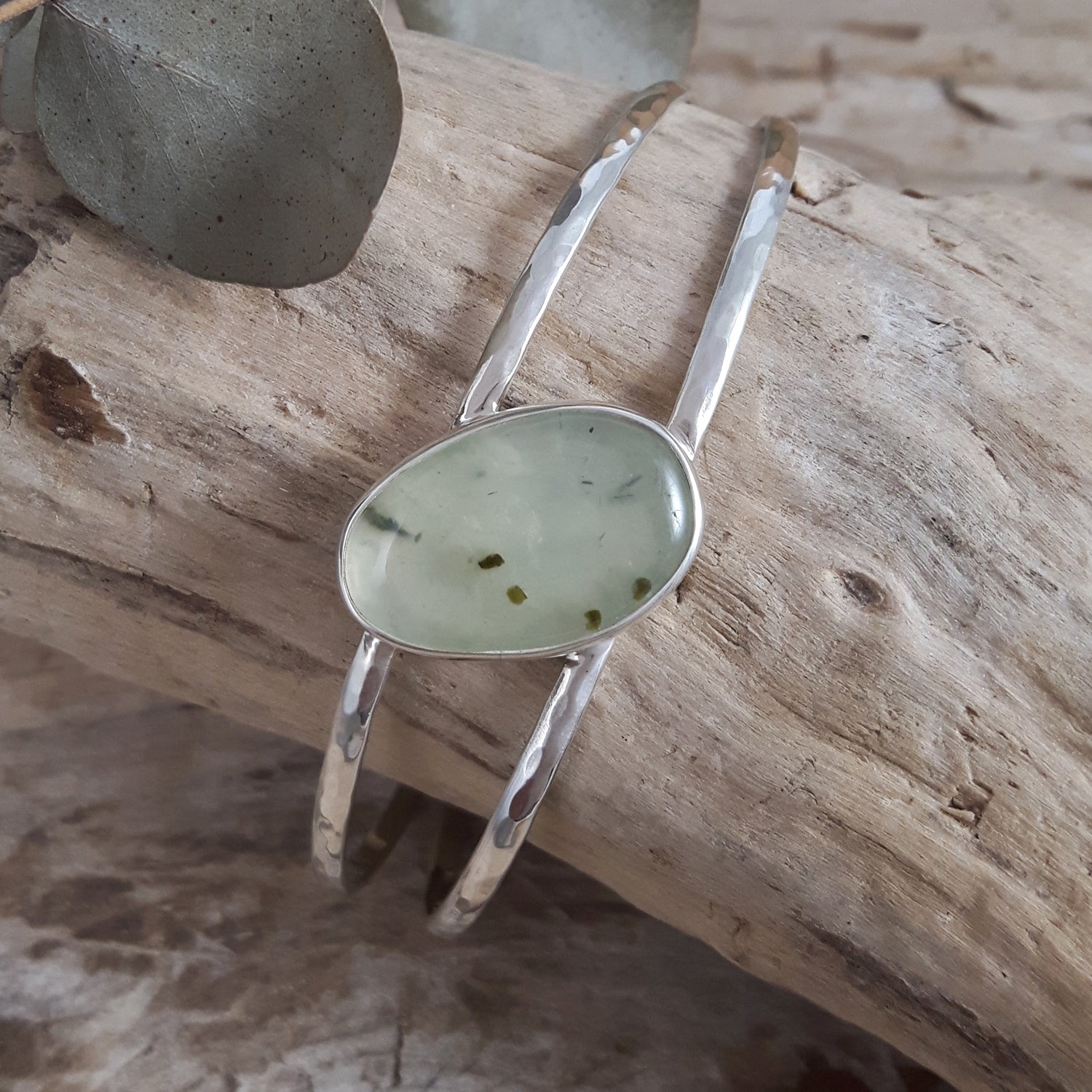 Sterling silver cuff with a green prehnite stone on a wooden surface