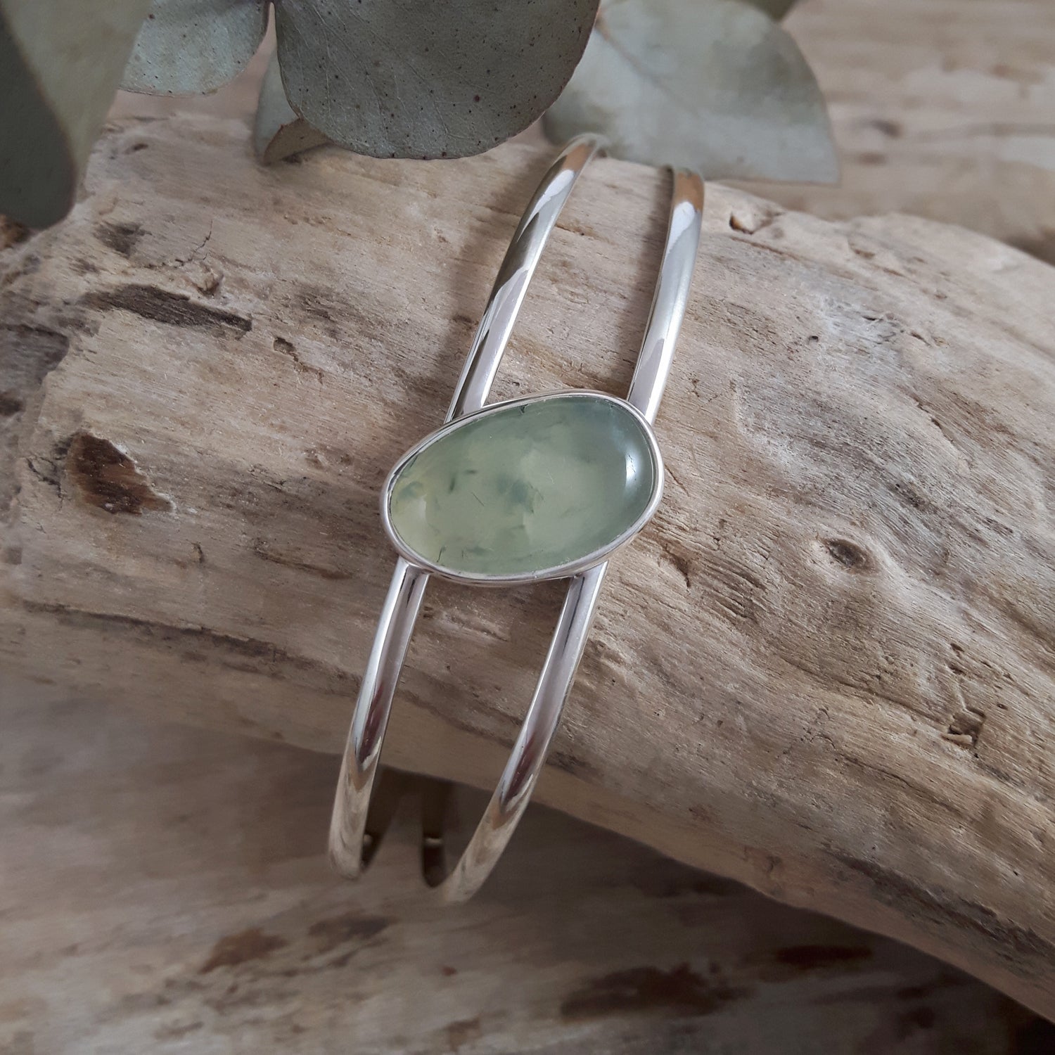 Sterling silver cuff bracelet with a green prehnite gemstone on a wooden surface