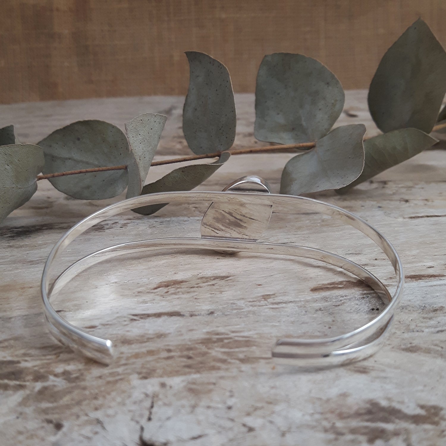 Sterling silver bracelet on a wooden surface with eucalyptus leaves