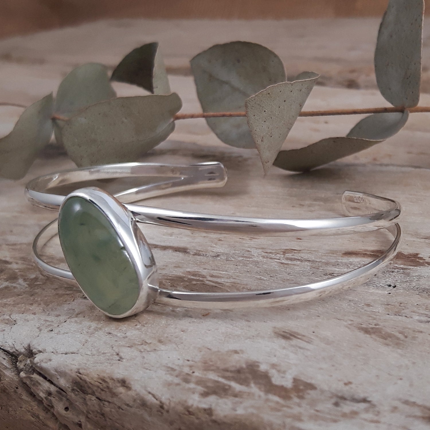 Sterling silver bracelet with a green prehnite stone on a wooden surface with leaves.