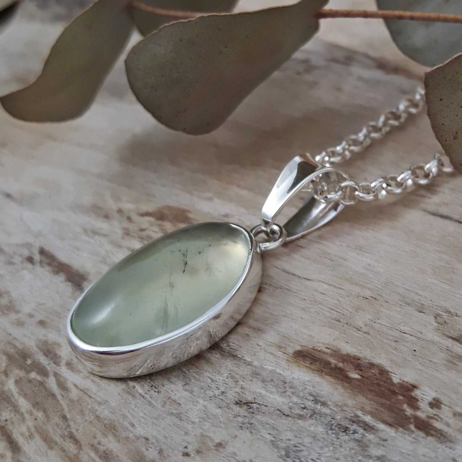 Sterling silver pendant with a green prehnite stone on a wooden surface with leaves in the background