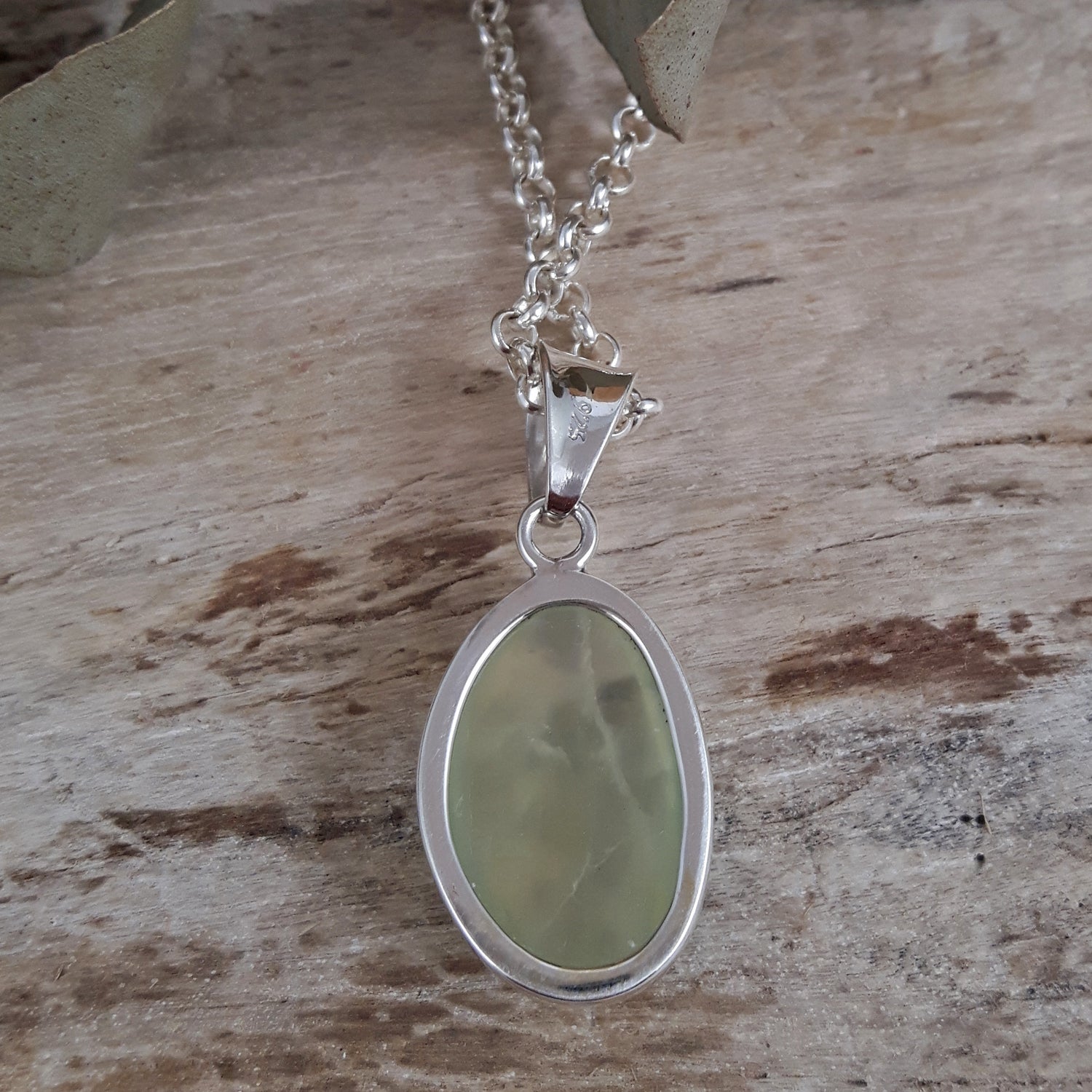 Back of a sterling silver pendant with a green prehnite stone on a wooden surface