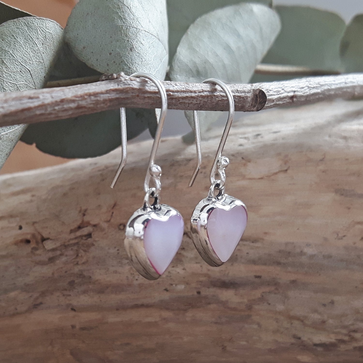 Heart-shaped mother-of-pearl drop earrings hanging from a branch with a natural background