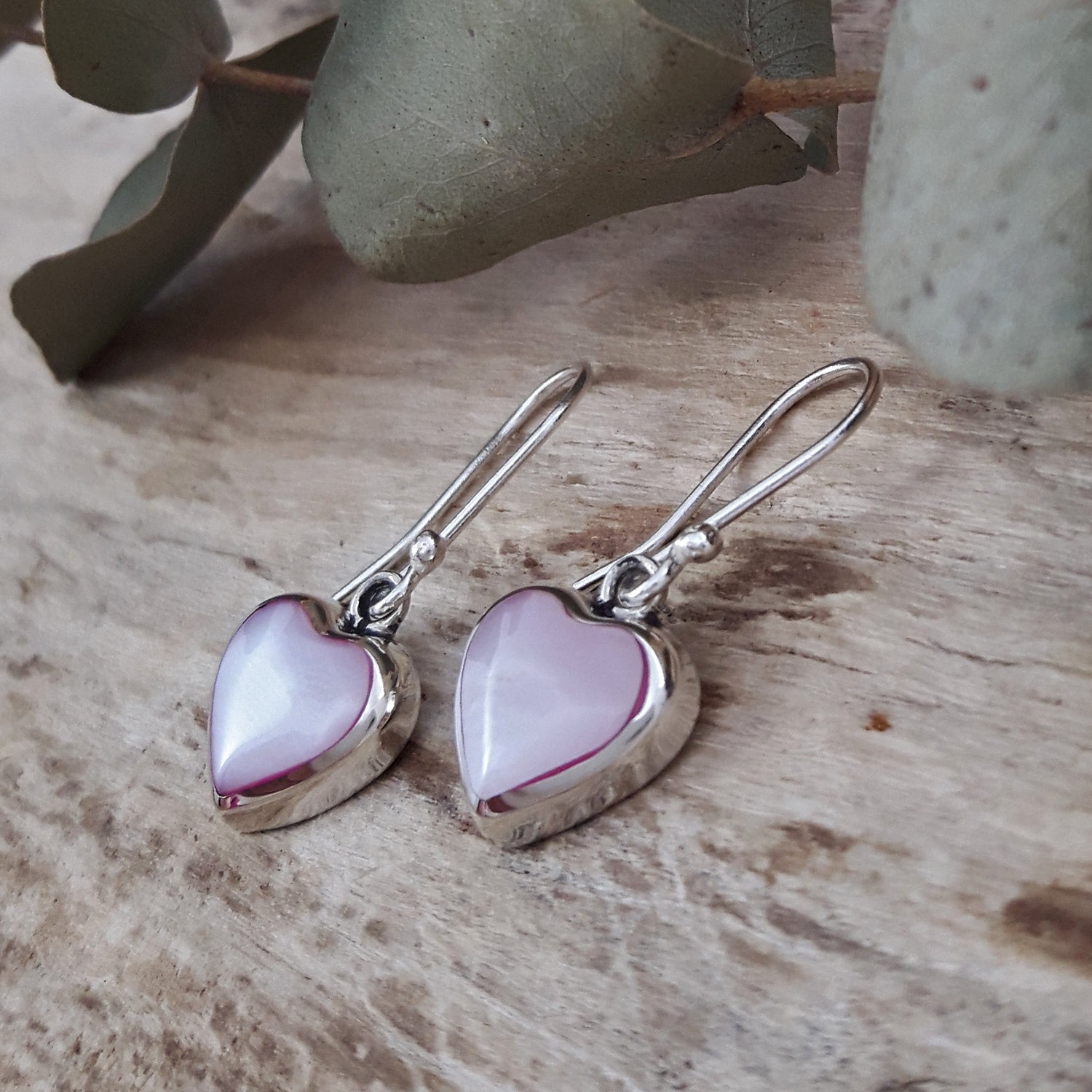 Heart-shaped earrings with pink mother-of-pearl on a wooden surface