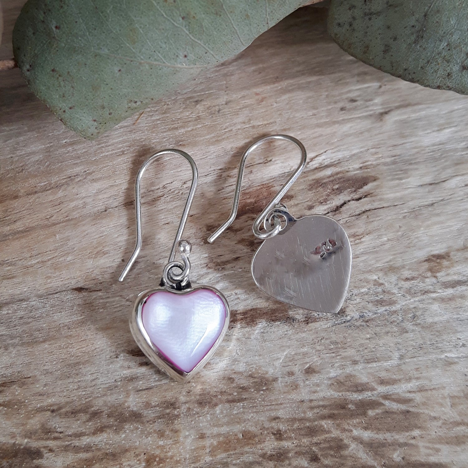 Heart-shaped earrings with pink center and silver heart on a wooden surface