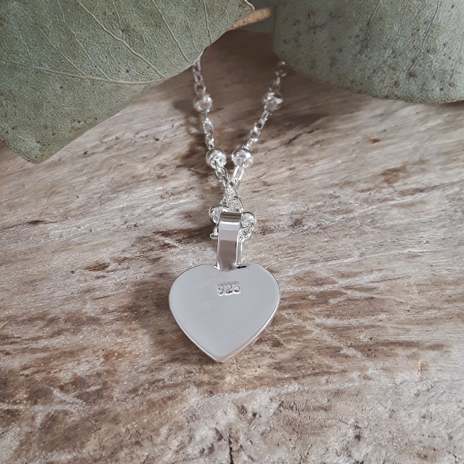 Silver necklace with a heart-shaped pendant on a wooden surface
