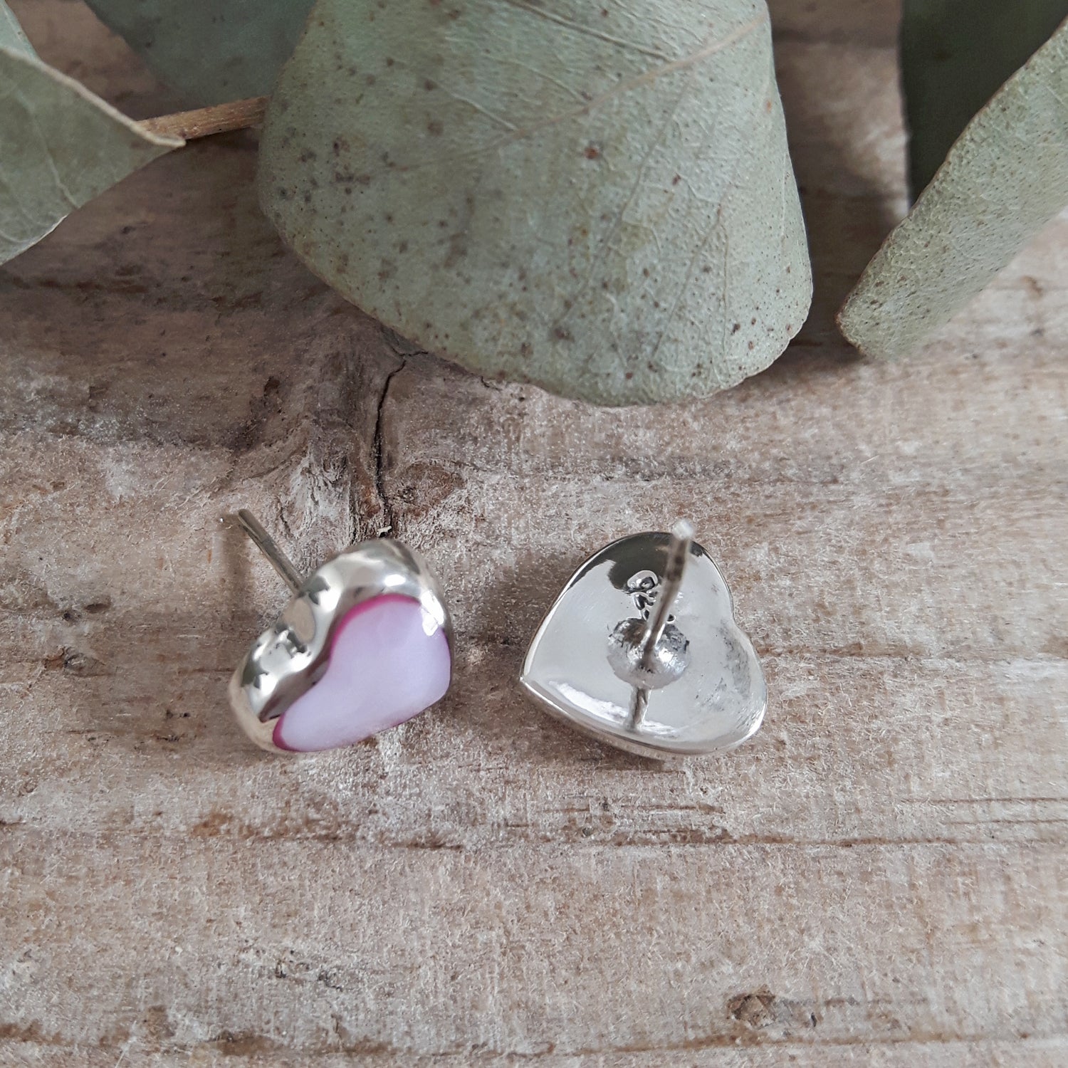 Heart-shaped silver earrings with pink interior on a wooden surface.