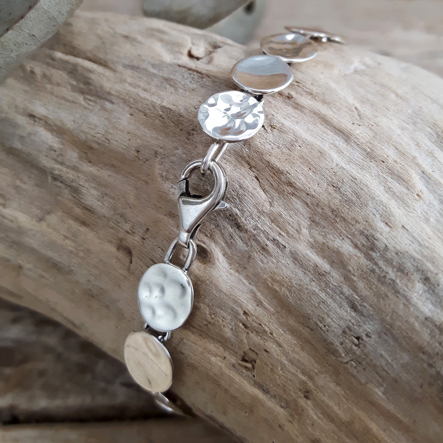 Silver bracelet with hammered and polished discs on a wooden surface