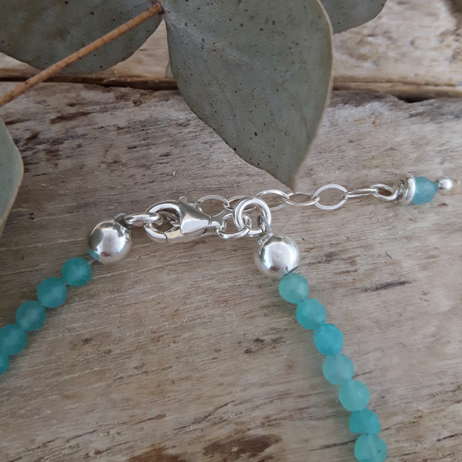 Silver bracelet with amazonite beads on a wooden surface with leaves.