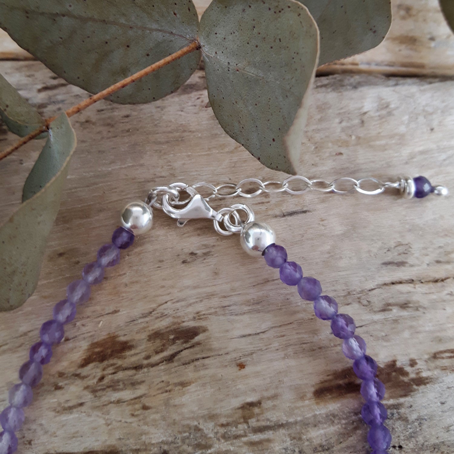 Sterling silver and amethyst beaded bracelet on a wooden surface with leaves in the background