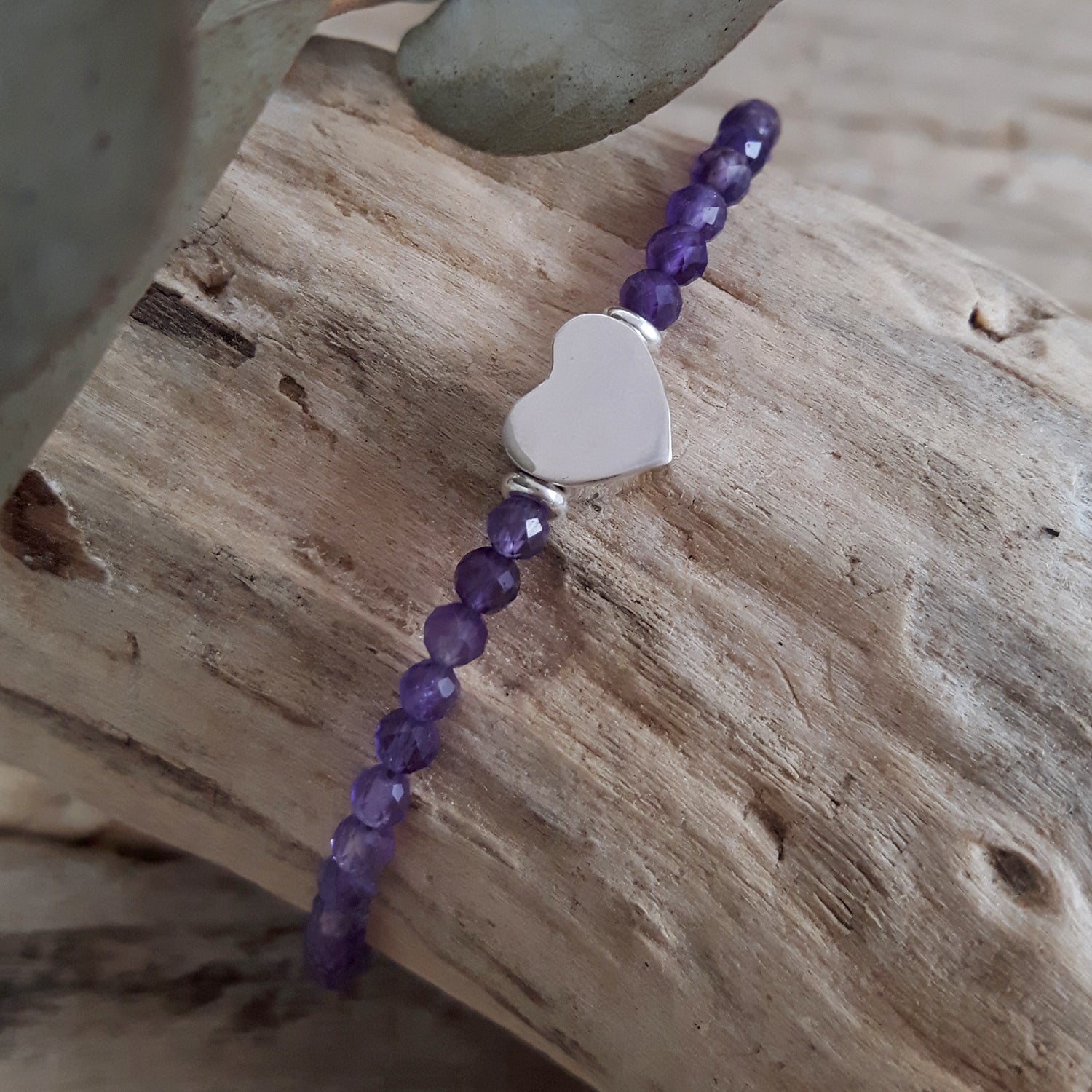 Bracelet with amethyst beads and a heart-shaped charm on wooden surface