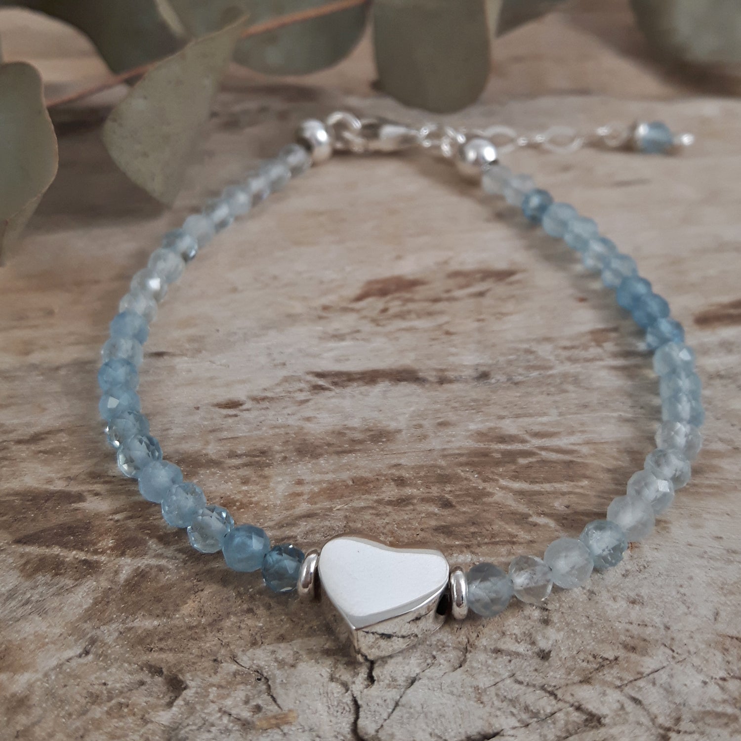 Bracelet with aquamarine beads and a sterling silver heart-shaped charm on a wooden surface