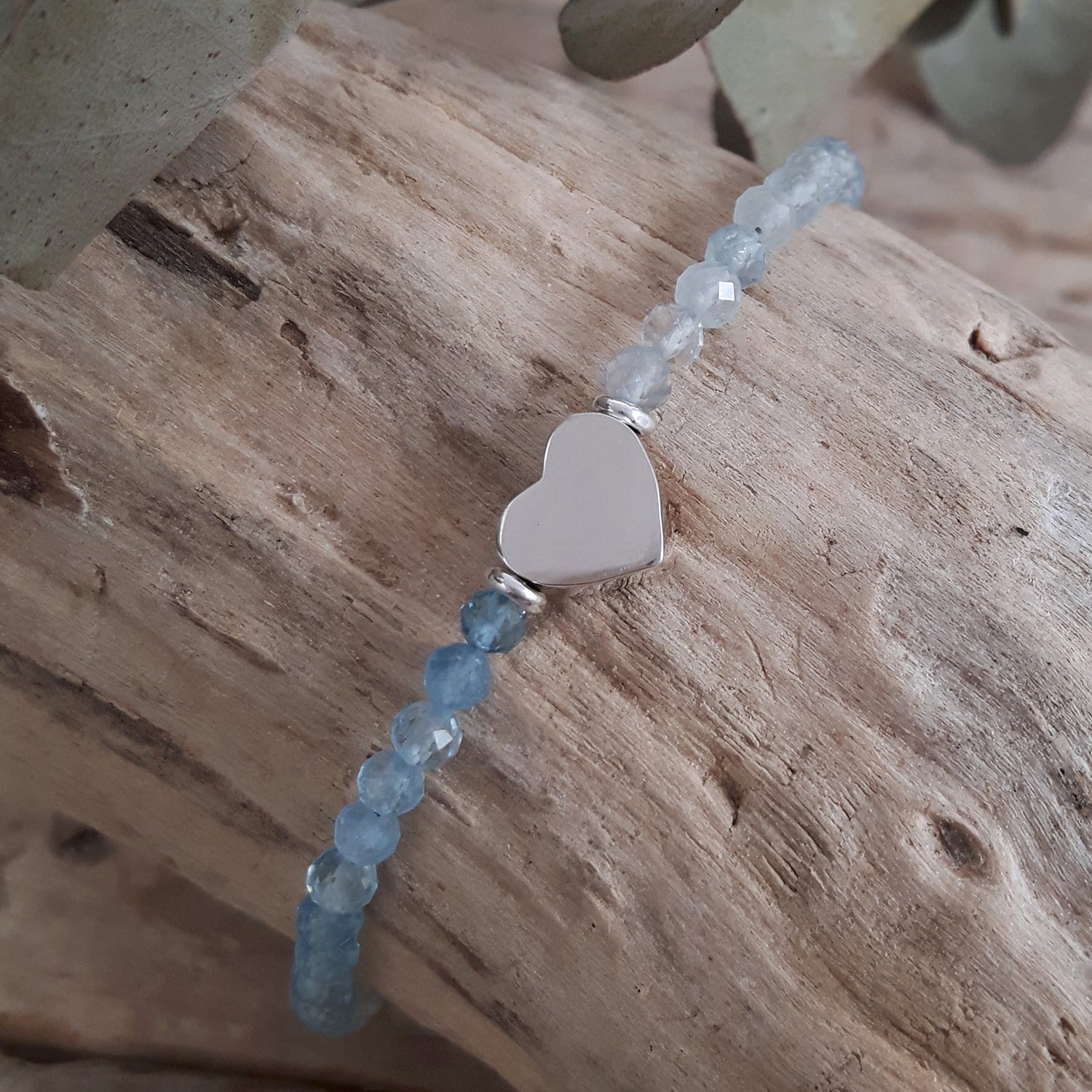 Bracelet with aquamarine beads and a sterling silver heart charm on wooden surface