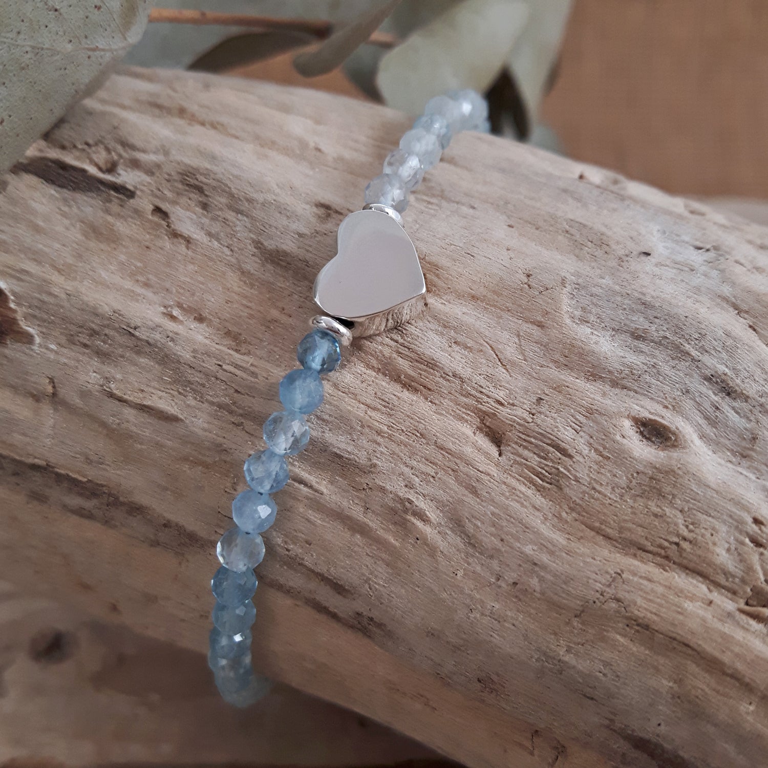 Aquamarine beaded bracelet with a sterling silver heart-shaped charm on a wooden surface