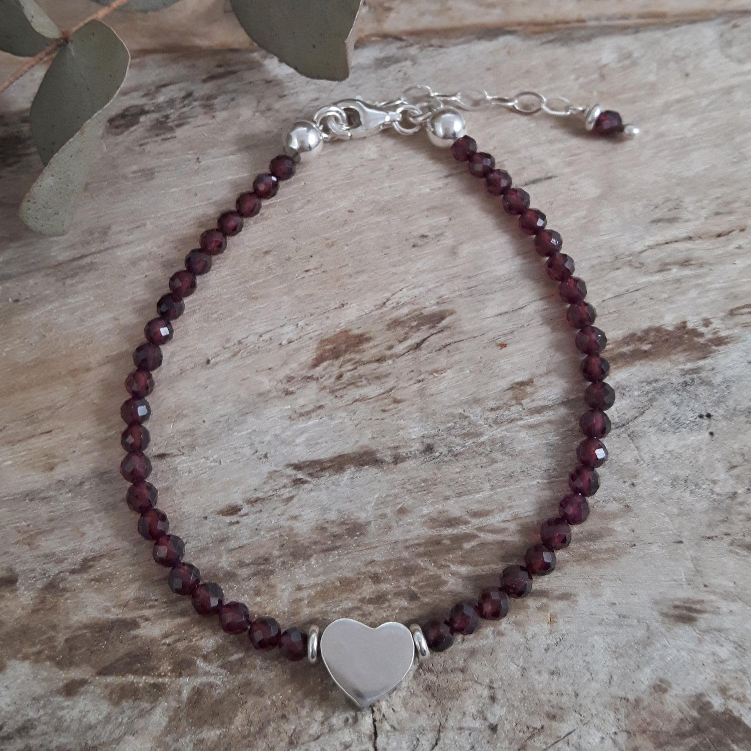 Garnet beaded bracelet with a heart charm on a wooden surface