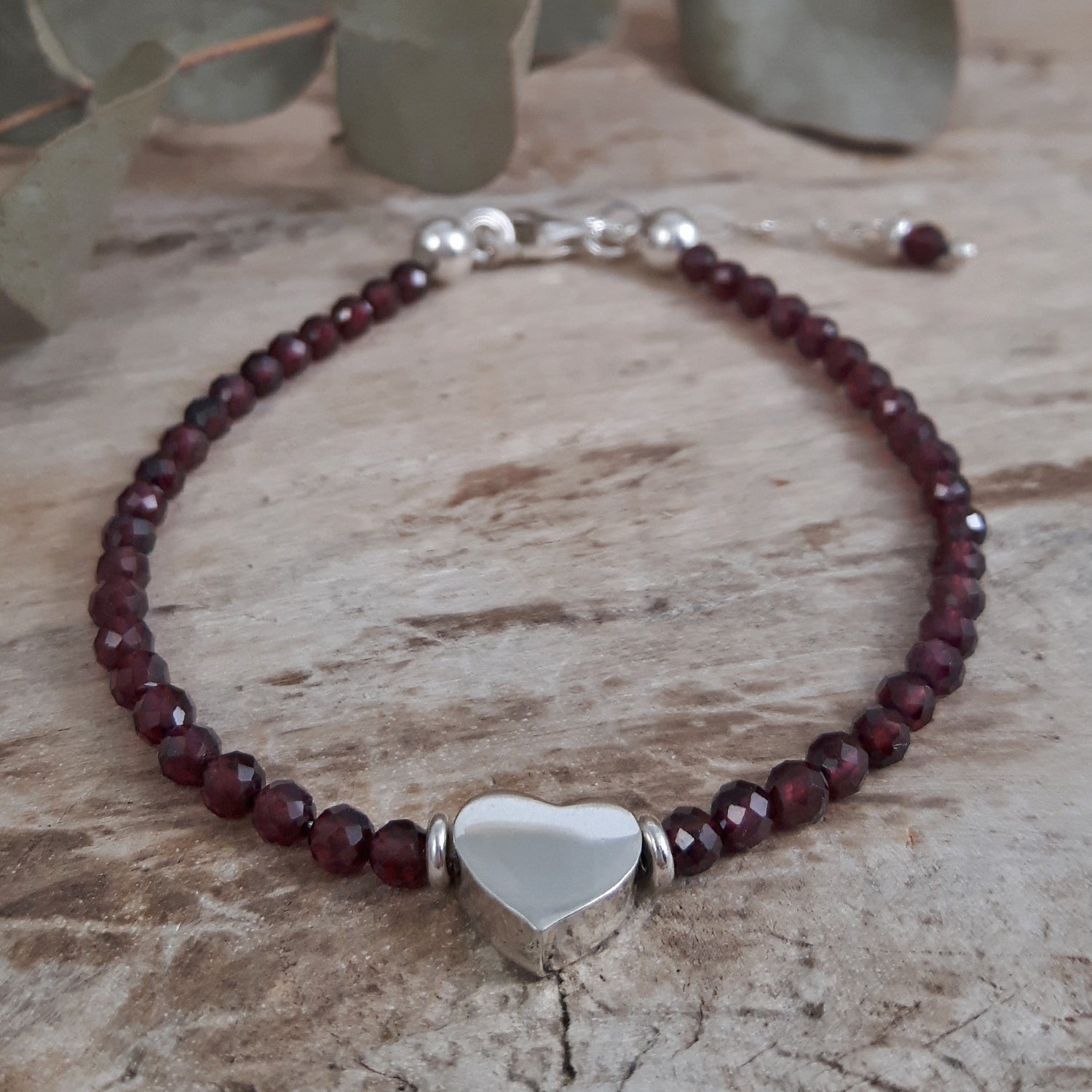 Birthstone bracelet with garnet beads and a silver heart charm on a wooden surface