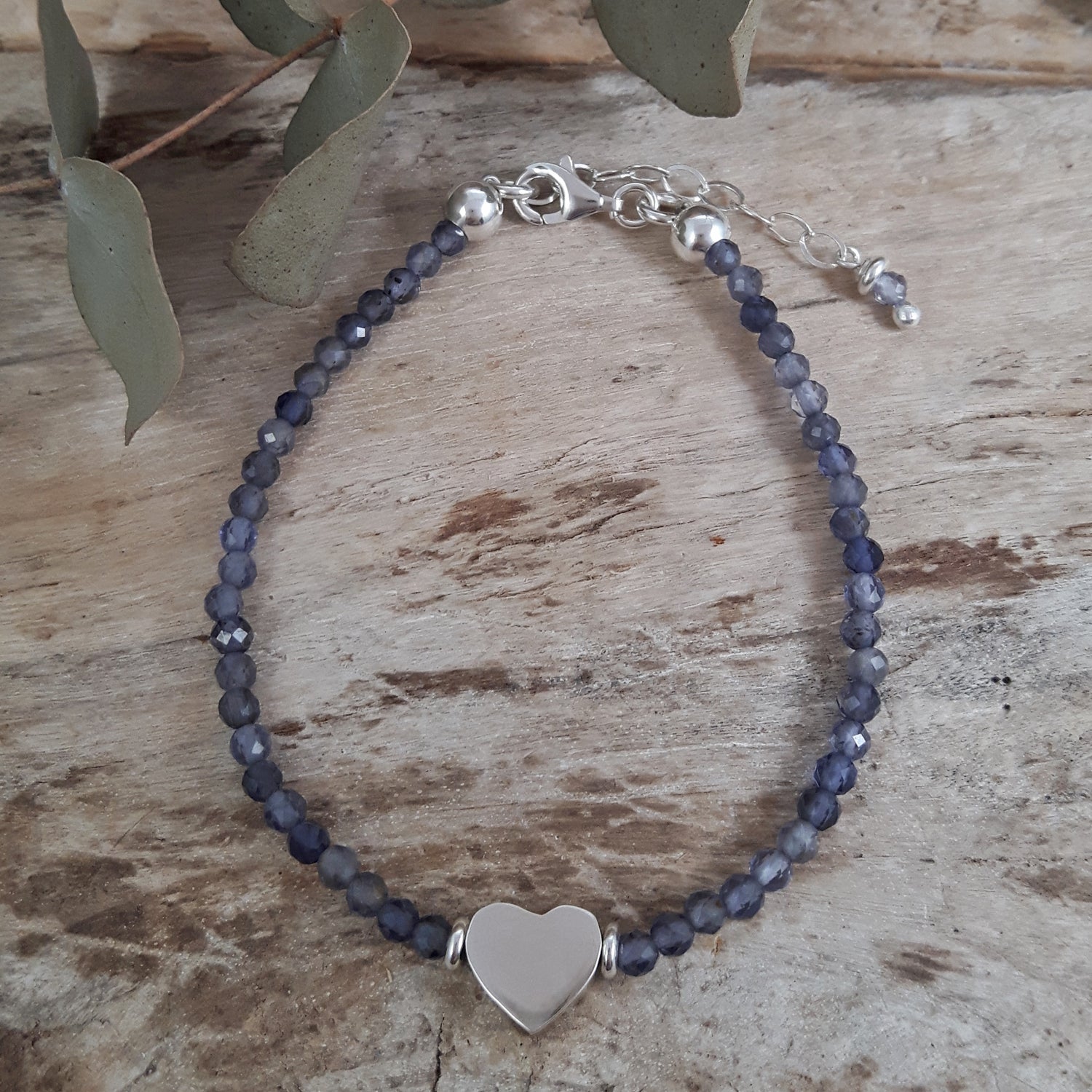Iolite birthstone beaded bracelet with a sterling silver heart charm on a wooden surface