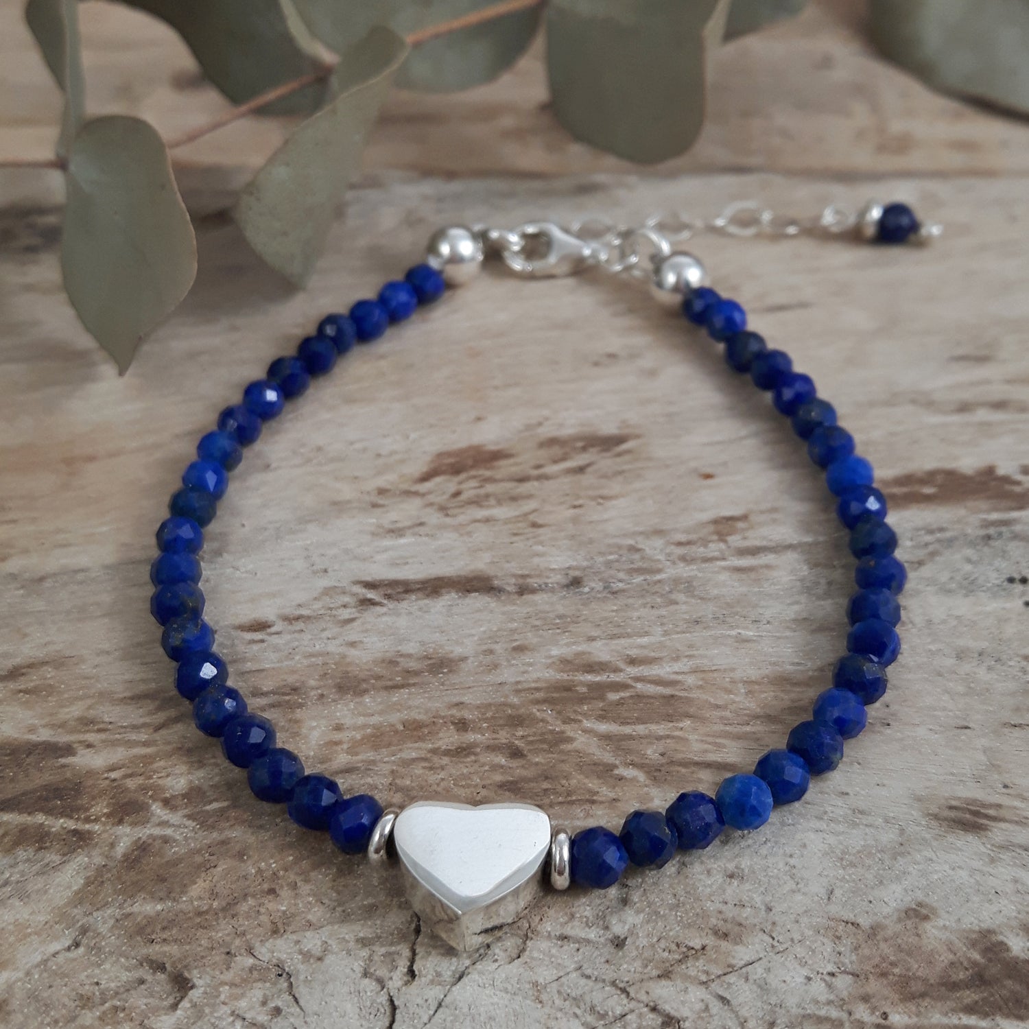 Blue lapis birthstone beaded bracelet with a sterling silver heart charm on a wooden surface