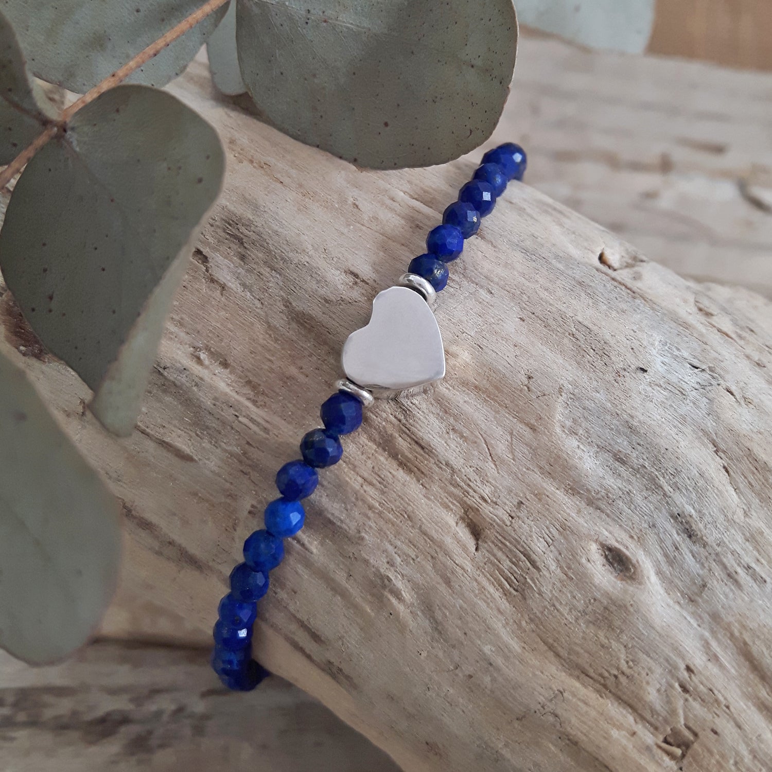 Blue lapis beaded birthstone bracelet with a sterling silver heart charm on a wooden surface