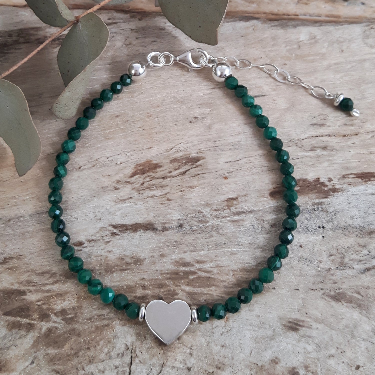 Malachite beaded bracelet with a sterling silver heart charm on a wooden surface.
