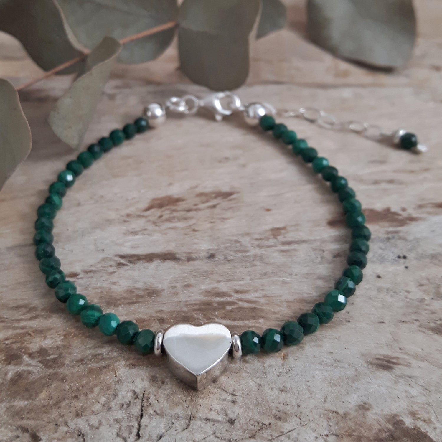 Malachite beaded bracelet with a sterling silver heart charm on a wooden surface.